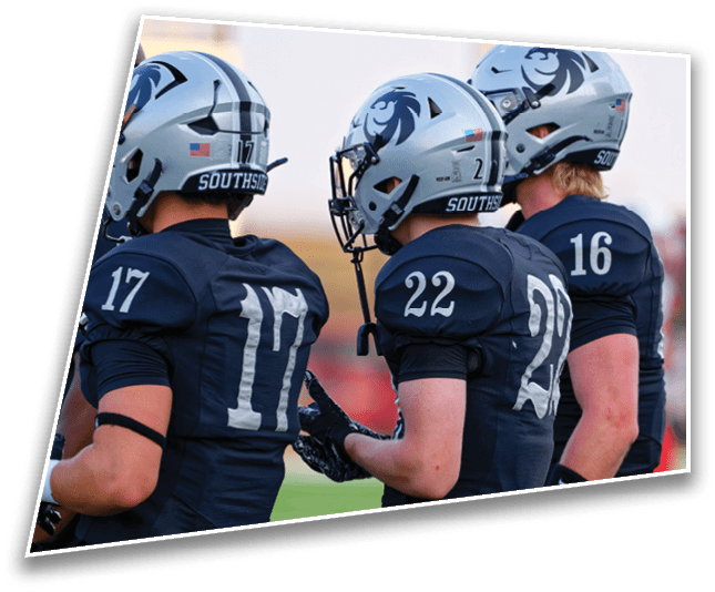 Three people wearing football helmets and dark uniforms with numbers on the back stand side by side on a field. Description generated by AI