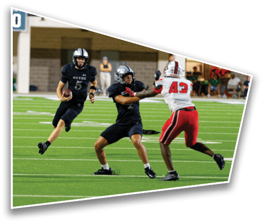 Three people in football uniforms are actively engaged on a green field with one person holding the ball while the others appear to be blocking or defending. Description generated by AI