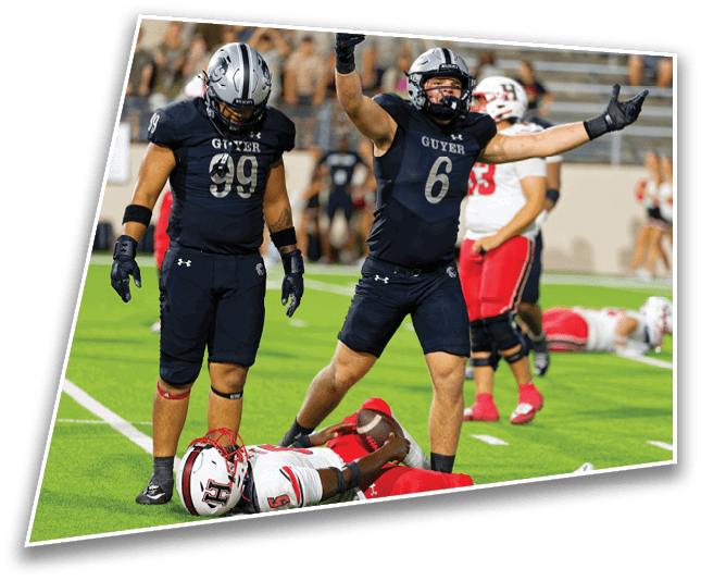 Two football players in dark uniforms celebrate on a field while a player in a white and red uniform lies on the ground during a game. Description generated by AI