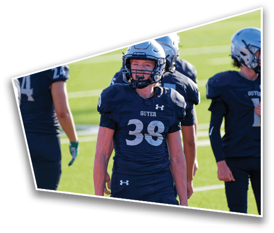 People wearing football uniforms with helmets stand on a grassy field during daylight. Description generated by AI