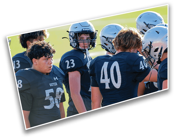 A group of people wearing dark football uniforms and helmets are gathered closely together on a field. Description generated by AI