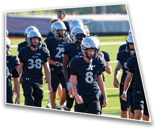 A group of people wearing black football uniforms and silver helmets are walking on a green field during daylight. Description generated by AI