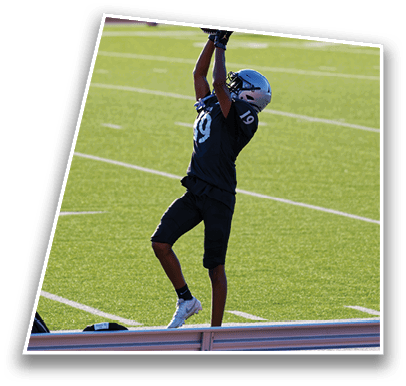 A person wearing a dark sports uniform and helmet is reaching up with both arms on a green football field near the sideline. Description generated by AI