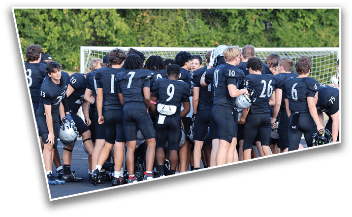 A group of people wearing black football uniforms are gathered together on a field near a goalpost with trees in the background. Description generated by AI
