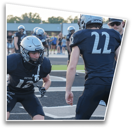 Two people in black football uniforms and helmets are positioned on a football field preparing for a play. Description generated by AI