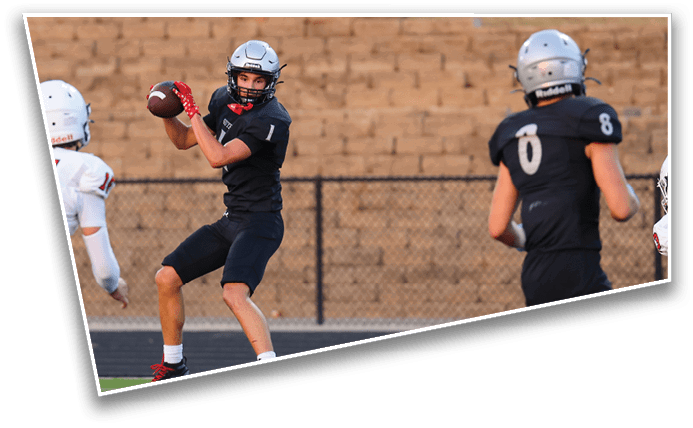 Two people in dark sports uniforms are on a field, with one preparing to throw a football and the other holding a football. Description generated by AI