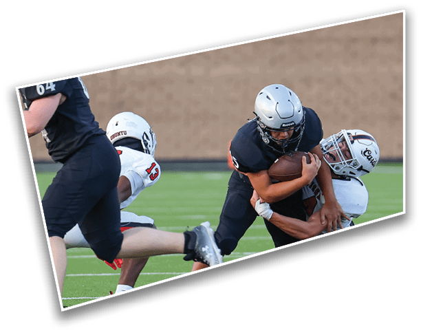 People in football uniforms are engaged in a tackle during a game on a grassy field. Description generated by AI