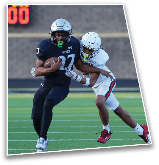 A person in a referee uniform is running on a football field behind a player in dark sports gear holding a football. Description generated by AI
