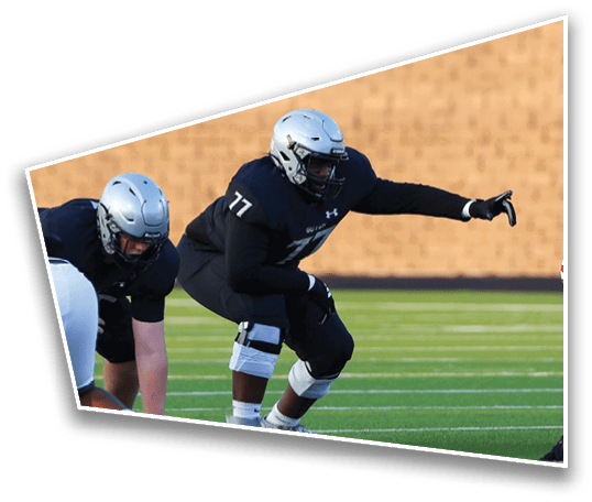 Two people in football uniforms and helmets are crouched in a ready position on a green field with yard lines. Description generated by AI