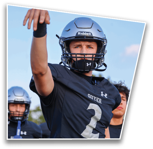 People wearing dark sports uniforms and helmets are standing outdoors, with one person raising an arm. Description generated by AI