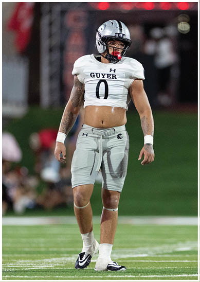 A person wearing a football uniform with the word “GUYER" and number zero on the jersey is standing on a football field. Description generated by AI