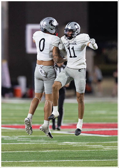 Two people wearing football uniforms and helmets are jumping and celebrating on a football field. Description generated by AI