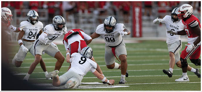 People in sports uniforms are actively playing on a grassy field, with one person sliding or falling near the ground. Description generated by AI