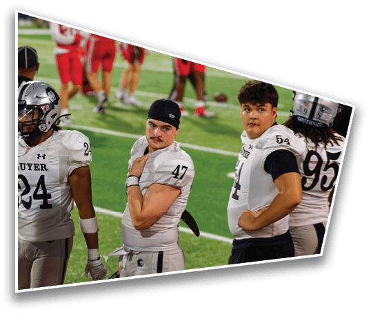 Four people wearing football uniforms stand on a field with some looking toward the camera and others facing away. Description generated by AI