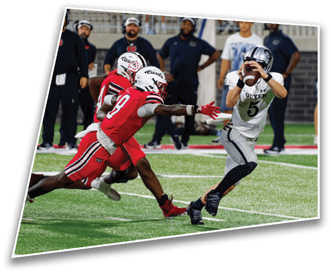 A person in a white and black football uniform is catching a football while two people in red uniforms are reaching out to tackle them on a football field with spectators in the background. Description generated by AI