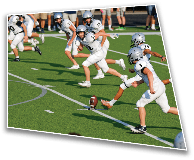 Several people in white football uniforms are running on a green field toward a football placed on a tee. Description generated by AI