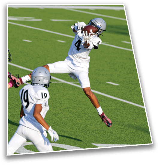 Two people in white football uniforms and helmets are on a green field with one person jumping to catch a football while the other watches. Description generated by AI