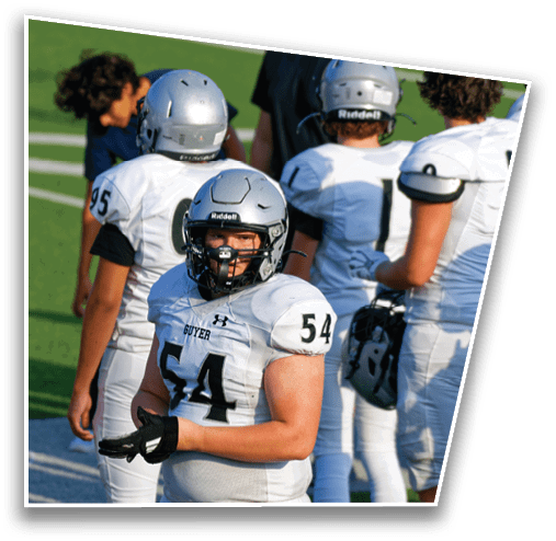 A group of people wearing white football uniforms and helmets stand on a green field, with one person in the foreground looking forward and wearing a jersey numbered 54. Description generated by AI