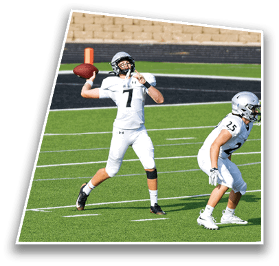 A person in a white football uniform is preparing to throw a football on a green field while another person in a similar uniform is positioned nearby. Description generated by AI