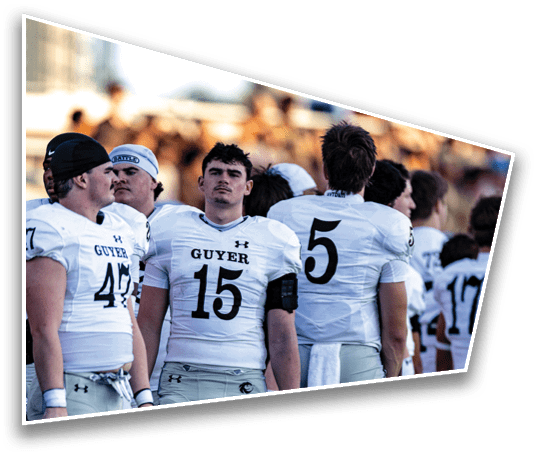 Several people wearing white football uniforms with the word “GUYER" and numbers on the front are standing together outdoors, appearing focused and attentive. Description generated by AI