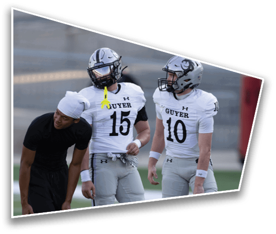 Three people wearing football helmets and jerseys with the word Guyer stand on a field, with one person in black athletic wear leaning forward. Description generated by AI