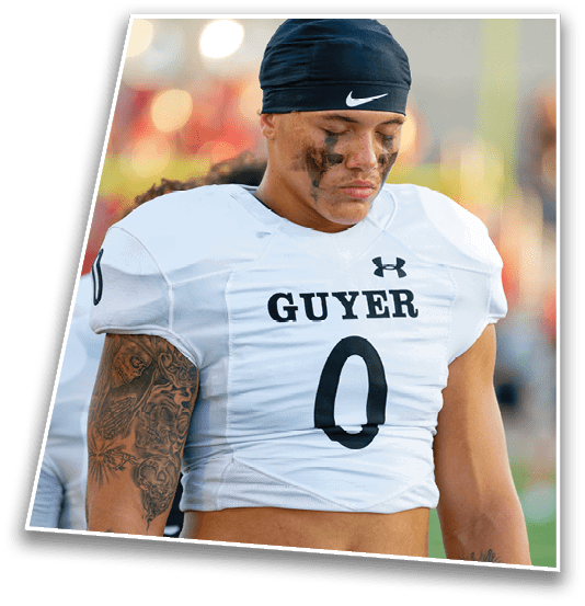 A person wearing a white football jersey with the word “GUYER" and the number zero on the front, along with black face paint and visible tattoos on their arms. Description generated by AI