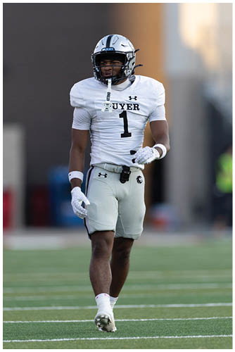 A person wearing white athletic shorts and gloves is walking on a green sports field with white yard lines. Description generated by AI