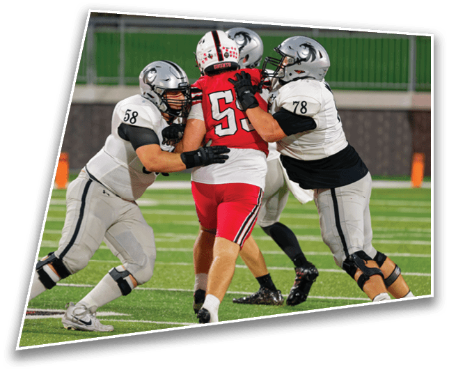 Two people in football uniforms are engaged in a blocking action on a football field during a game. Description generated by AI