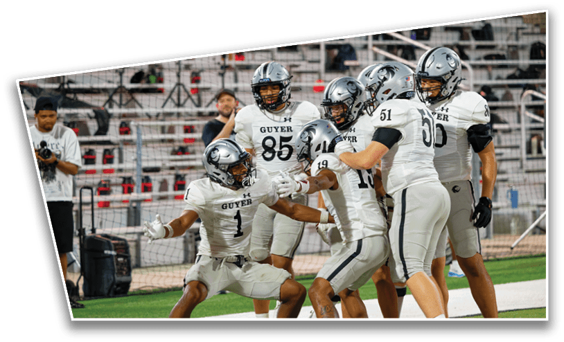 A group of football players in white and gray uniforms with helmets are celebrating on a field with empty bleachers in the background. Description generated by AI