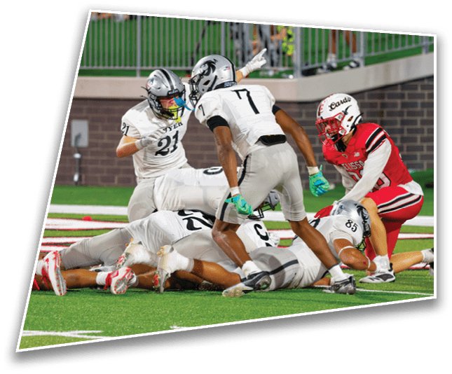 Several people in football uniforms are engaged in a play on a green field with one person in red kneeling near a group of people in white uniforms who are on or near the ground. Description generated by AI