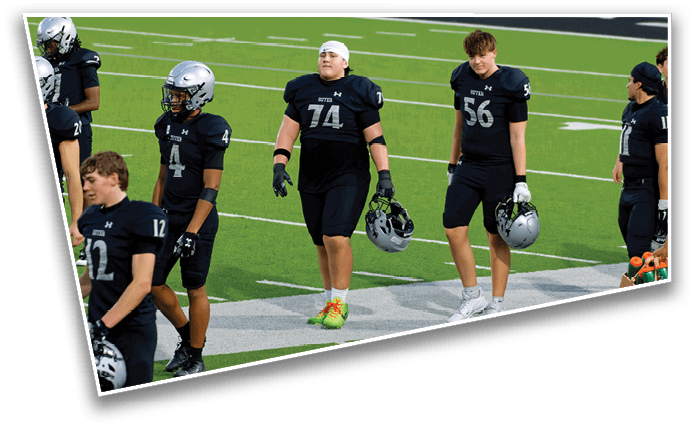 People wearing black football uniforms and helmets are standing and walking on a green football field. Description generated by AI