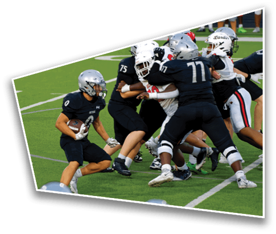 A group of people wearing football uniforms are engaged in a play on a green field with one person holding the ball and others blocking or tackling. Description generated by AI
