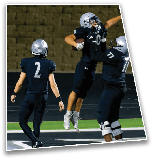 Two people wearing football helmets and uniforms are on a field with one person holding a football. Description generated by AI
