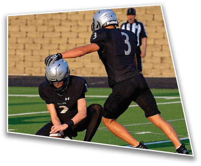 A person wearing a silver helmet and black sports jersey with the number 3 is on a field with a blurred referee in the background. Description generated by AI