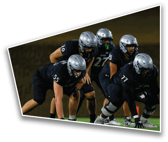 Four people in football uniforms and helmets are positioned on a field, appearing ready for a play during a game. Description generated by AI
