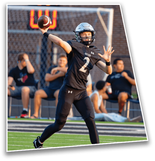 A person wearing a football helmet and black uniform with the number 2 is in the motion of throwing a football on a field with spectators in the background. Description generated by AI