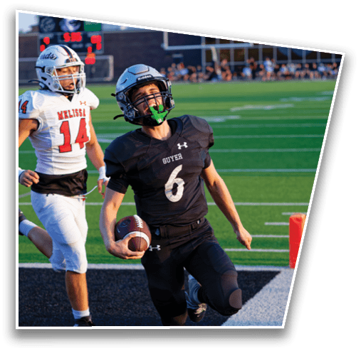 A person in a black football uniform is running with the ball toward the end zone while two people in white football uniforms chase behind on a green field. Description generated by AI