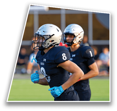 Two people wearing football helmets and dark uniforms with numbers 8 and 1 are running on a field during a game. Description generated by AI
