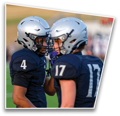 Two people wearing football helmets and dark jerseys with numbers 4 and 17 are standing on a football field engaged in conversation. Description generated by AI
