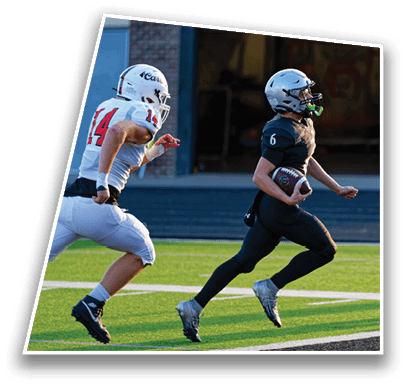 A person in black athletic gear and helmet is running with a football toward the end zone while another person in white sportswear chases behind on a football field. Description generated by AI