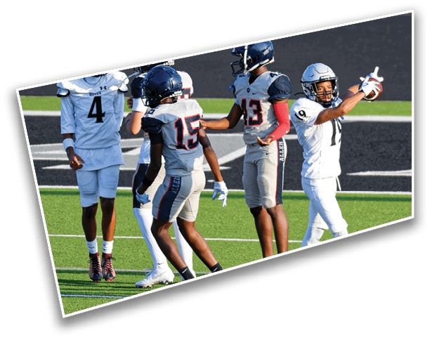 Five people in football uniforms stand on a green field with black and white markings, with one person in white celebrating with raised arms. Description generated by AI