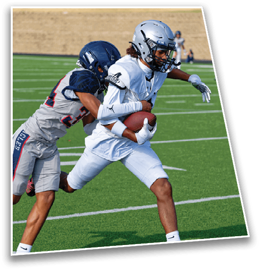 Two people in football gear are on a field with one person holding the ball while the other attempts to tackle them. Description generated by AI