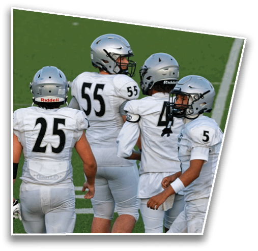 Three people wearing white football uniforms and silver helmets stand on a green field, with two facing away and one looking to the side. Description generated by AI