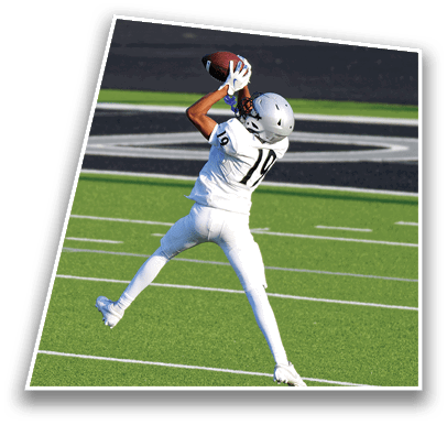 A person wearing a white football uniform and helmet is catching a football on a green field near the end zone. Description generated by AI