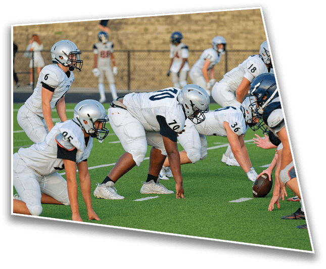 Players in football uniforms are lined up on a green field preparing for a play during a game. Description generated by AI