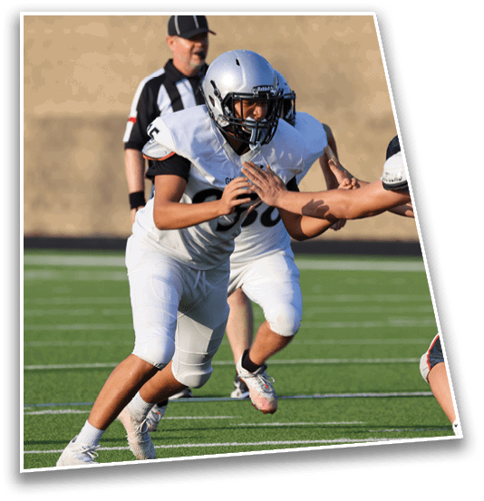 Three people in football uniforms are engaged in a play on a green field with one person attempting to block another who is running with the ball. Description generated by AI