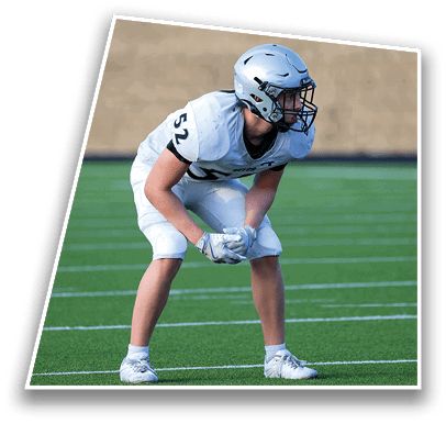 A person wearing a white football uniform and helmet is crouched in a ready position on a green football field. Description generated by AI