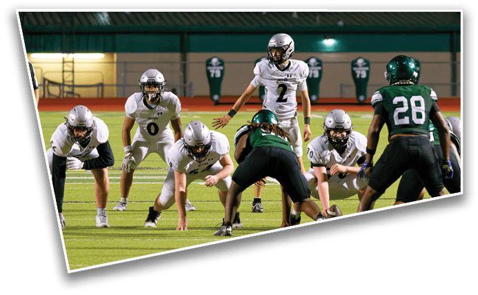 People in football uniforms are lined up on a field preparing for a play during a game. Description generated by AI