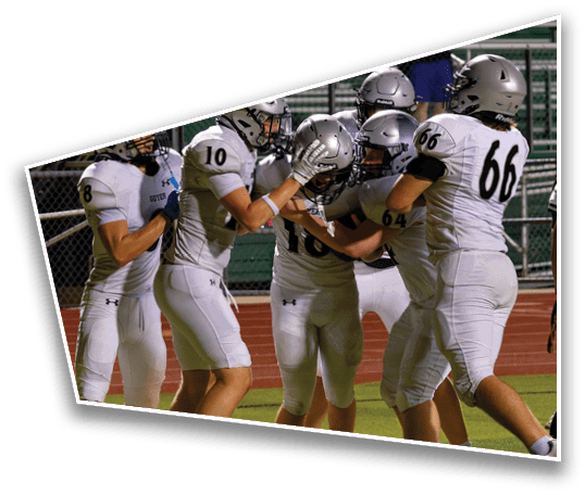 A group of people wearing white football uniforms and helmets are gathered closely on a field, appearing to celebrate or support each other. Description generated by AI