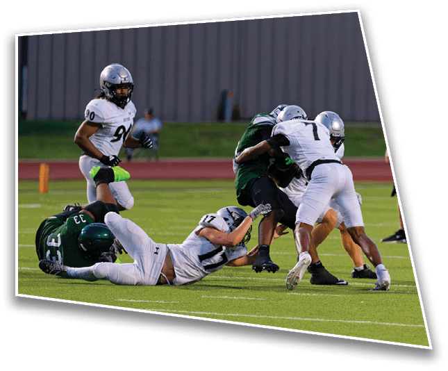 Several people in football uniforms are engaged in a tackle on a grassy field while a referee watches nearby. Description generated by AI